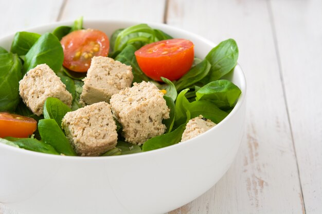 Salada de tofu vegan em tigela com tomate e alface de cordeiro na mesa de madeira branca