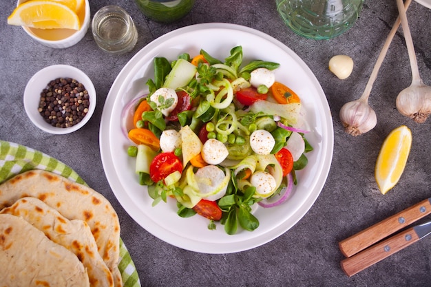 Salada de tomate cereja fresco, mussarela, manjericão e outras verduras na mesa de jantar com pão pita achatado