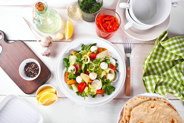 Salada de tomate cereja fresco, mussarela, manjericão e outras verduras na mesa de jantar com pão pita achatado