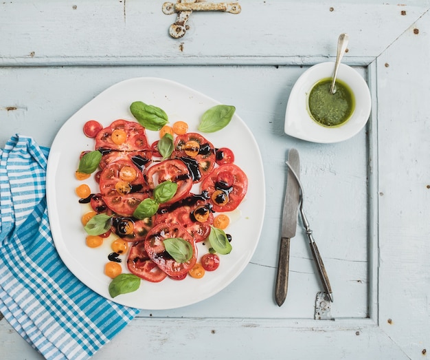 Salada de tomate da vila madura com azeite e manjericão sobre fundo azul de madeira claro