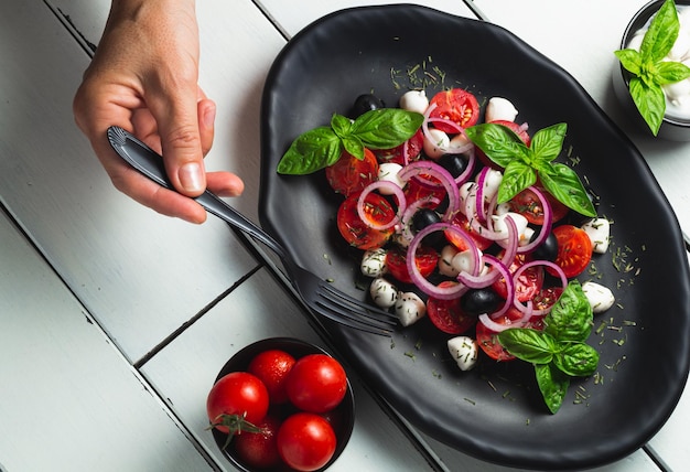 Foto salada de tomate e mozzarella caprese e molho de pesto com azeitonas em mesa branca servida com garfo