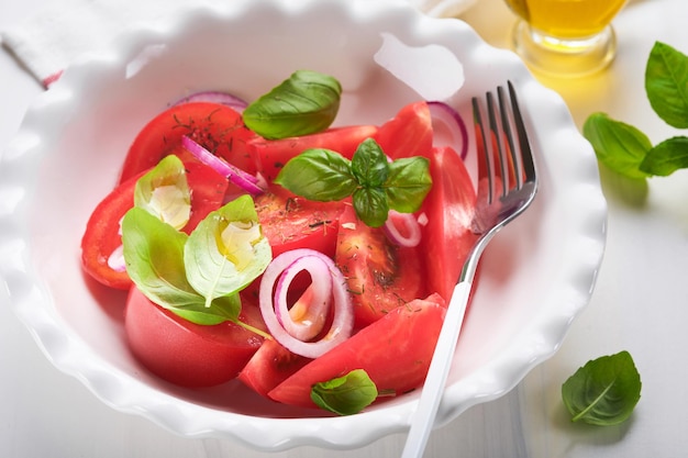 Salada de tomate fresco com folhas de manjericão azeite e cebola em tigela branca sobre fundo claro Dieta tradicional italiana ou mediterrânea Vista superior