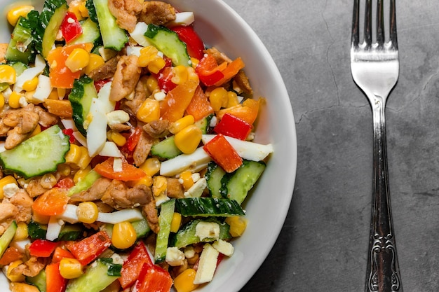 Salada de vegetais brilhantes com frango em um fundo cinza de concreto. Fazendo uma deliciosa salada para uma alimentação saudável. Salada de legumes para nutrição adequada em uma tigela e um garfo