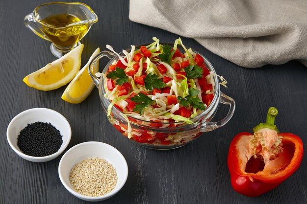 Foto salada de vegetais de repolho ralado e páprica com molho de limão e azeite de oliva adornado com salsa e salpicado com cominho e sementes de gergelim em uma mesa de concreto preto
