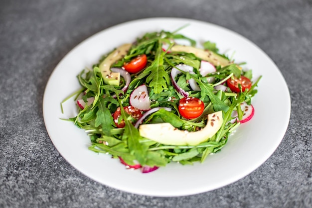 Salada de vegetais frescos saudáveis tomates rúcula abacate rabanete em um fundo de pedra