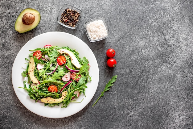 Salada de vegetais frescos saudáveis tomates rúcula abacate rabanete em um fundo de pedra