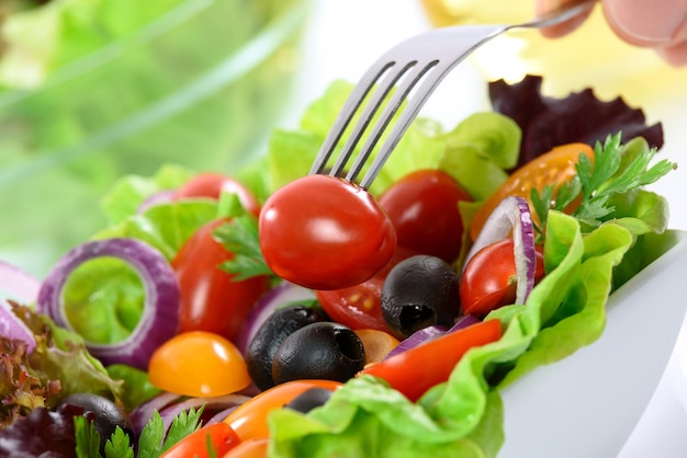 Salada de vegetais mista de nutrição saudável em uma tigela sobre a mesa e uma mão segurando um garfo com tomate