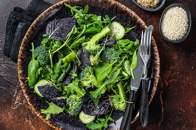 Salada de vegetais saudável com folhas frescas de rúcula, alface, espinafre para salada vegan. Fundo escuro. Vista do topo.