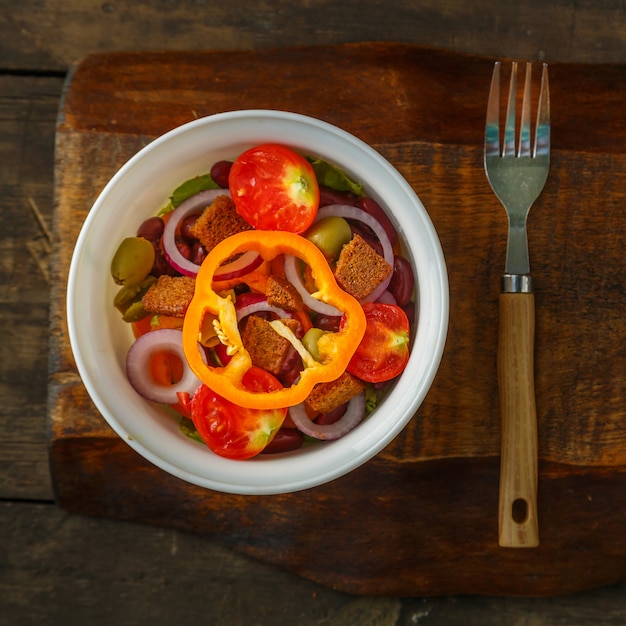 Salada de vegetais saudável em uma saladeira em uma mesa de madeira ao lado de um garfo.