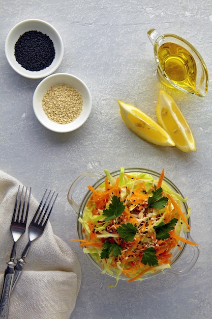 Salada de verão leve de repolho branco e cenouras com gergelim e sementes de cominho preto em uma tigela de vidro