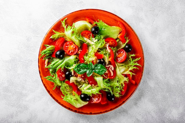 Salada de verão simples de tomates de alface com azeitonas e azeite em um prato vermelho e cinza claro