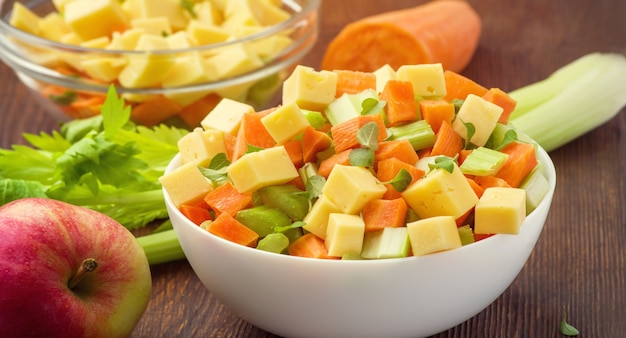 Salada de vitamina de talos de aipo, cenoura, maçã e queijo. Salada de legumes com queijo cortado em cubos em um prato e uma série de ingredientes são.