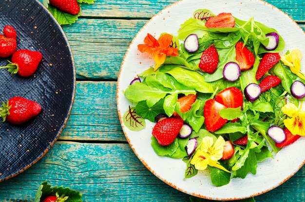 Salada de vitaminas com morangos, espinafre, capuchinha e rúcula. Salada vegana verde. Vista superior na mesa de madeira