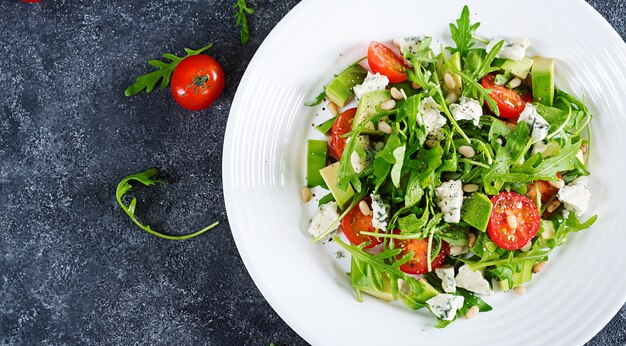 Salada dietética com tomates, queijo azul, abacate, rúcula e pinhões. Vista do topo. Lay plana.