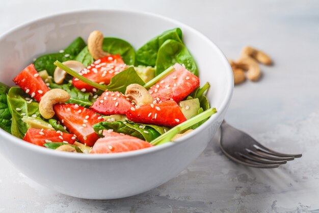 Salada do abacate da morango do verão com cajus em uma bacia branca.