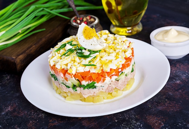 Salada do fígado de bacalhau com ovos, pepinos, batatas, cebola verde e cenoura em uma placa.