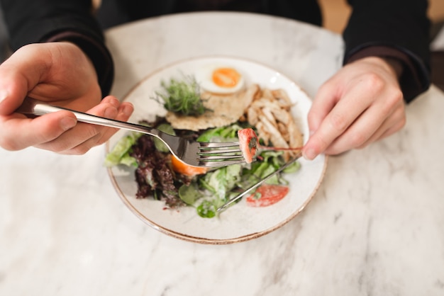 Salada e mãos com uma faca e um garfo close-up, vista superior. Um homem come uma salada em um restaurante.