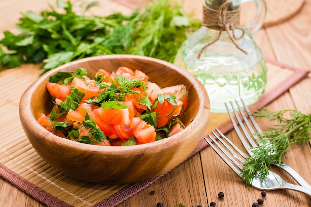 Salada feita de tomates e ervas frescas, óleo vegetal e garfo na mesa de madeira
