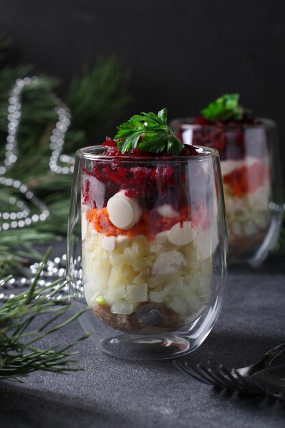 Salada festiva russa tradicional Herring sob um casaco de pele em copos com porções em um fundo cinza escuro