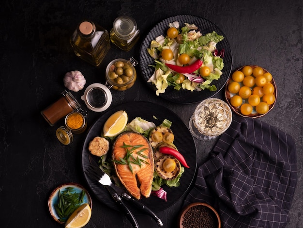 Salada de filete de salmón a la parrilla con verduras aceitunas y vino sobre fondo negro Vista superior de primer plano Pescado rojo con ajo tomate amarillo y especias en plato negro Concepto de comida saludable y dietética