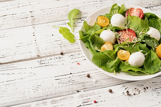 Salada fresca com queijo mussarela de tomate cereja rúcula e queijo duro sobre fundo branco de madeira Vista superior