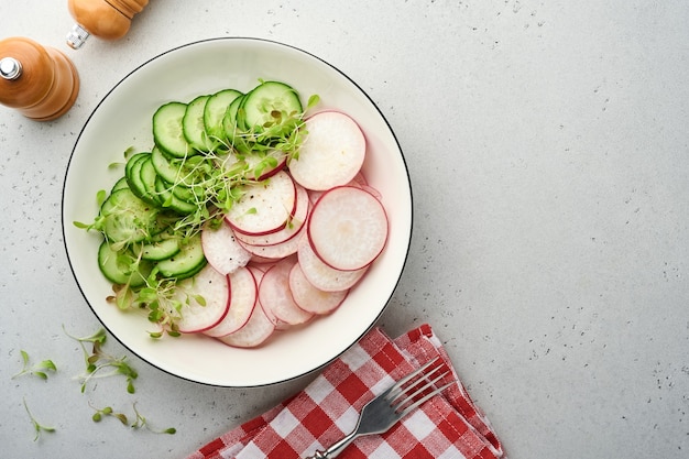 Salada fresca com rabanete vermelho, pepino, legumes, rabanetes microgreen em chapa branca sobre fundo de pedra cinza. Vista de cima. Conceito vegan e alimentação saudável.