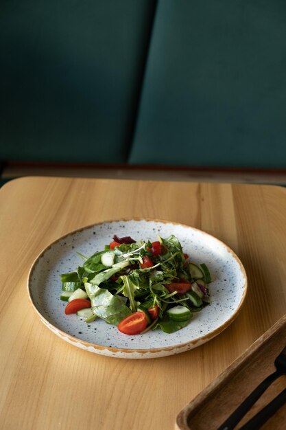 Salada fresca com rúcula, tomate, cereja, pepinos num prato contra o interior do café