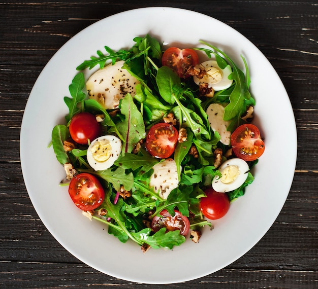 Salada fresca com tomate, verduras, nozes, ovos, sobre fundo de madeira. Comida saudável.