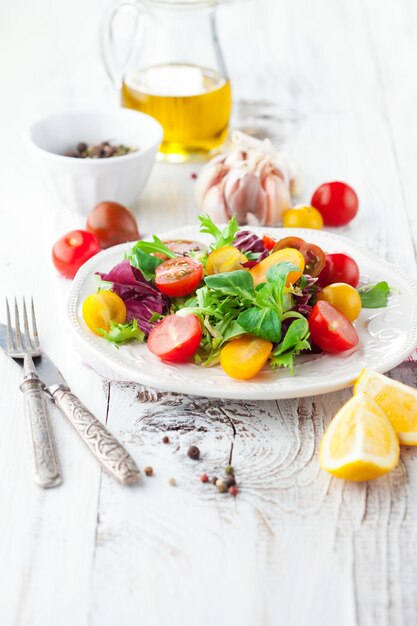 Foto salada fresca com tomates cereja espinafre rúcula romana e alface em um prato sobre fundo de madeira branca