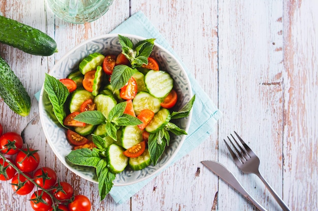 Salada fresca de pepino, tomate cereja e folhas de hortelã em uma tigela sobre a mesa
