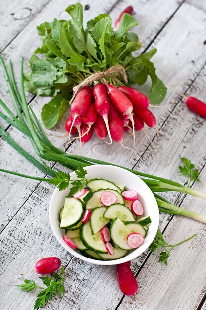 Salada fresca de pepinos e rabanetos em uma tigela branca sobre o antigo fundo de madeira