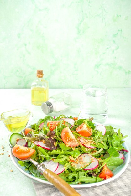 Salada fresca de primavera colorida com tomate, abacate, nozes, pepino, rabanete de primavera, no espaço da cópia de fundo verde claro. conceito de comida saudável de dieta de primavera