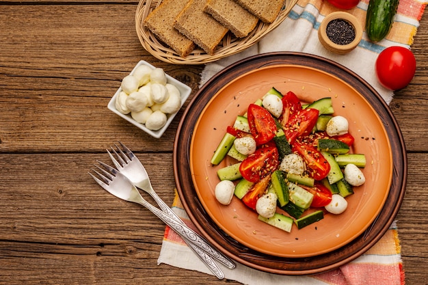 Salada fresca de tomate, pepino e mussarela de bebê. Almoço ensolarado com pão duro