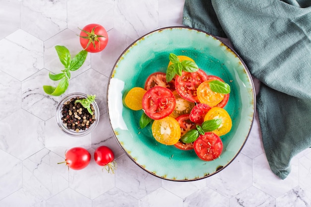 Salada fresca de tomates amarelos e vermelhos com folhas de manjericão em um prato na mesa Vista superior