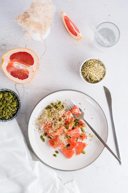 Salada fresca de trevo de toranja e brotos de alfafa e sementes de abóbora e talheres em um prato na mesa Comida de desintoxicação vegetariana orgânica Vista superior e vertical