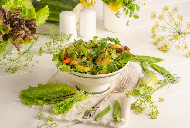 Salada fresca de verão com cenoura abobrinha e ervas em uma tigela sobre uma mesa de madeira clara