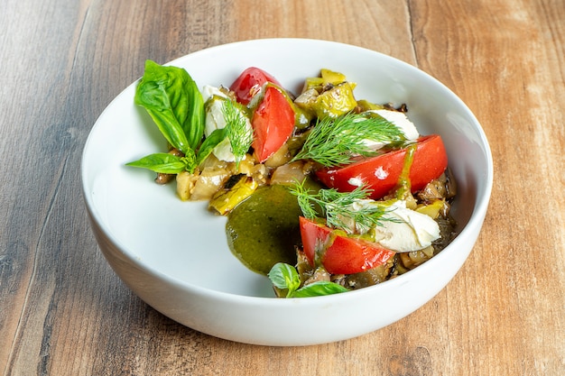 Salada fresca do vegetariano com vegetais cozidos na bacia do whte no fundo de madeira. Alimento saudável e equilibrado para atletas e dieta.