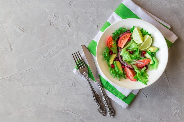 Salada fresca e saudável com tomate, abacate e romã em uma tigela sobre fundo claro de concreto