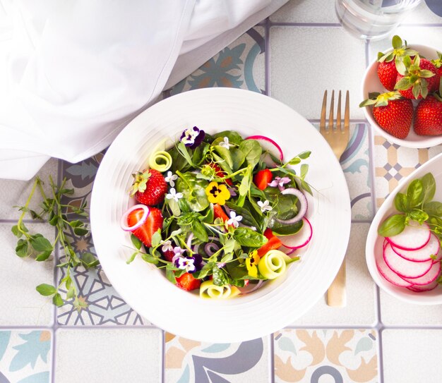 Salada fresca saudável de primavera com flores verdes comestíveis amores-perfeitos viola e morangos