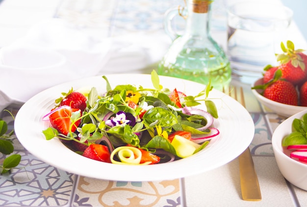 Salada fresca saudável de primavera com flores verdes comestíveis amores-perfeitos viola e morangos