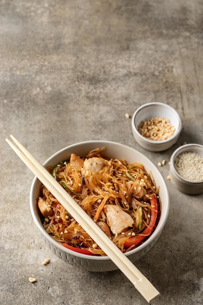 Salada funchose asiática com frango e legumes em tigela com pauzinhos e molho com ingredientes em fundo verde texturizado com espaço de texto Menu de comida