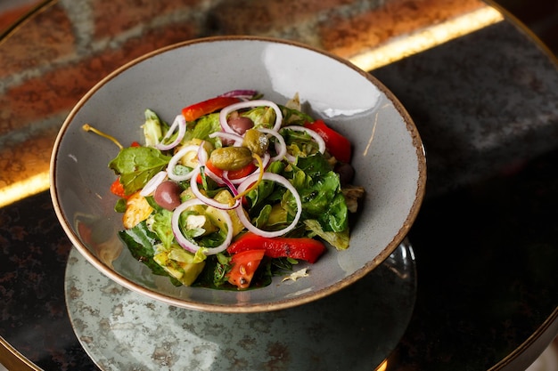 Salada grega com legumes frescos tomate pepino pimentão vermelho alface cebola azeitonas e queijo Closeup em um prato redondo branco sobre um fundo de madeira Menu de saladas com ingredientes