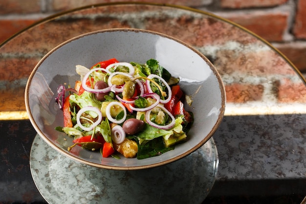 Salada grega com legumes frescos tomate pepino pimentão vermelho alface cebola azeitonas e queijo closeup em um prato redondo branco sobre um fundo de madeira menu de saladas com ingredientes