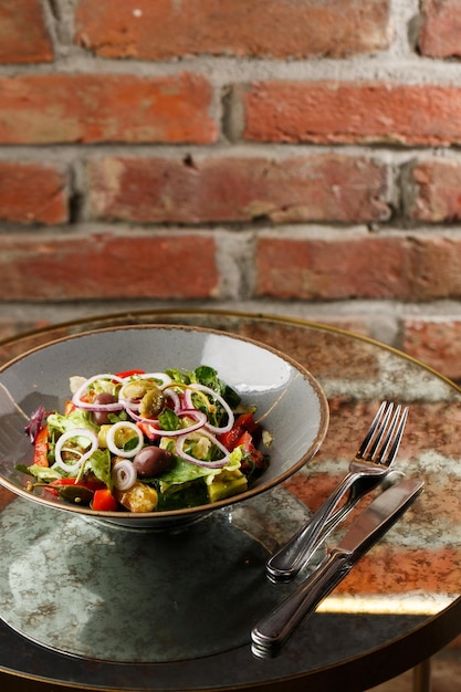 Salada grega com legumes frescos tomate pepino pimentão vermelho alface cebola azeitonas e queijo Closeup em um prato redondo branco sobre um fundo de madeira Menu de saladas com ingredientes