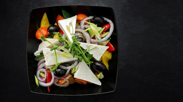 Salada grega com queijo e legumes em um prato preto