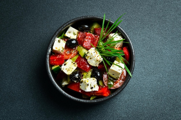 Salada grega com queijo feta em uma tigela preta em um close de fundo escuro