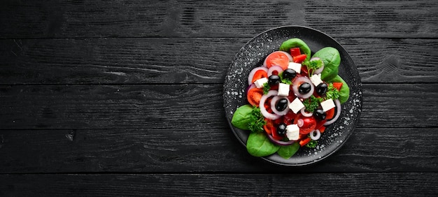 Salada grega com tomate, cebola, páprica e queijo feta Em um prato preto sobre um fundo de madeira Vista superior Espaço livre para o seu texto Postura plana
