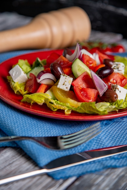 Salada grega de pepino fresco, tomate, pimentão, alface, cebola roxa, queijo feta e azeitonas com azeite de oliva na madeira. comida saudável