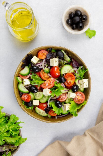 Salada grega fresca com tomate cereja, pepino, alface, azeitona preta, queijo feta e óleo de azeitonas em superfície cinza clara