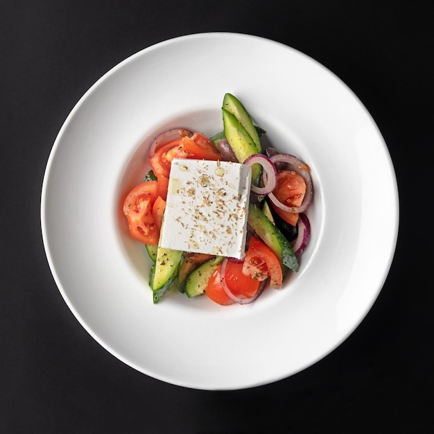 Salada grega fresca, queijo feta, tomate, pepino, pimenta vermelha, azeitonas pretas e cebola em um fundo preto